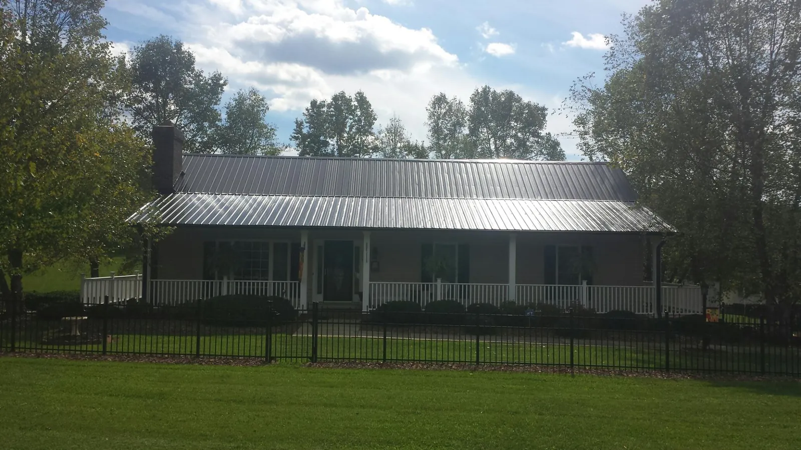 Gray metal roof on a brick ranch with a full width front porch — Gutter Guard Installation work by our crew in Lansing